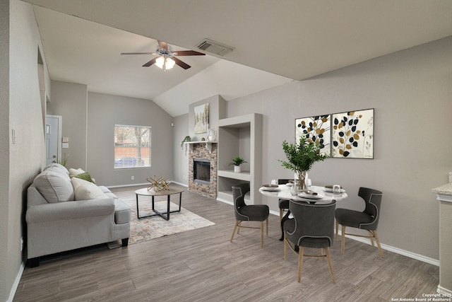 living room featuring vaulted ceiling, a stone fireplace, wood finished floors, and visible vents