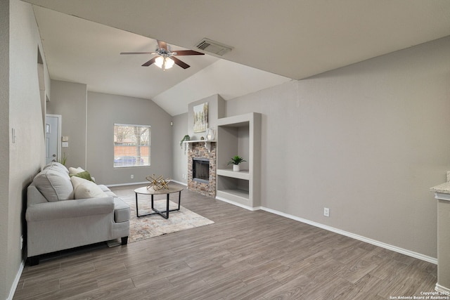 living area featuring visible vents, a ceiling fan, wood finished floors, vaulted ceiling, and a fireplace