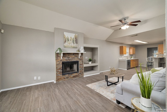 living room featuring ceiling fan, a stone fireplace, light wood finished floors, and baseboards