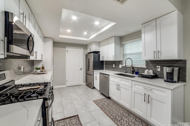 kitchen with a sink, appliances with stainless steel finishes, a raised ceiling, and white cabinets