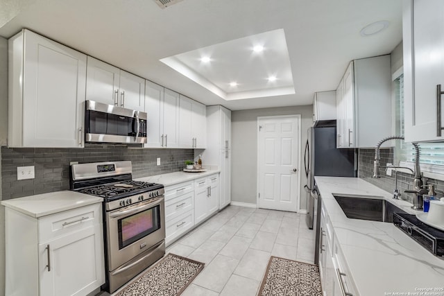 kitchen with light stone countertops, a tray ceiling, stainless steel appliances, white cabinetry, and a sink