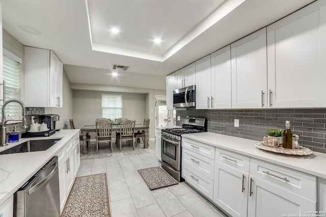 kitchen with appliances with stainless steel finishes, a tray ceiling, white cabinets, and a sink