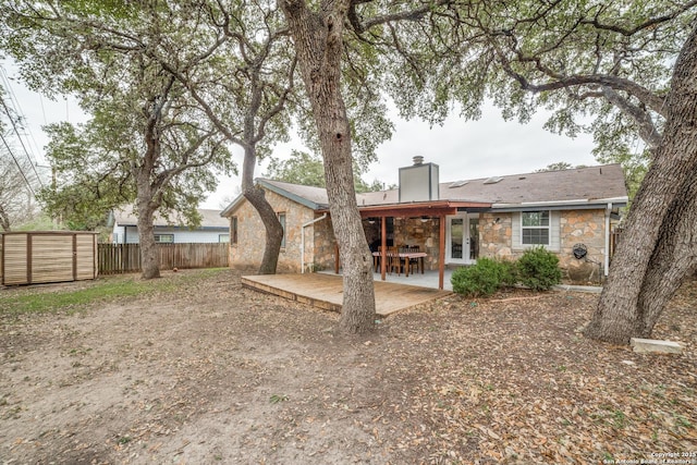 rear view of property featuring stone siding, a chimney, fence, and a patio