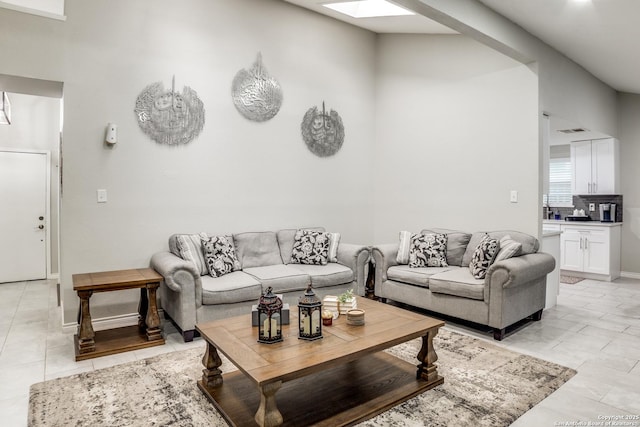 living area with light tile patterned flooring, a skylight, and baseboards