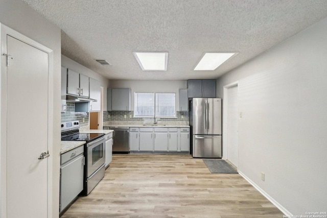 kitchen with under cabinet range hood, stainless steel appliances, light countertops, gray cabinets, and decorative backsplash