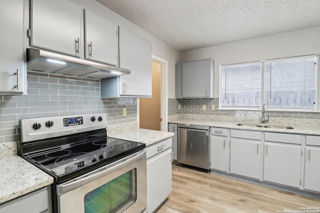 kitchen featuring appliances with stainless steel finishes, a textured ceiling, light wood-type flooring, under cabinet range hood, and a sink