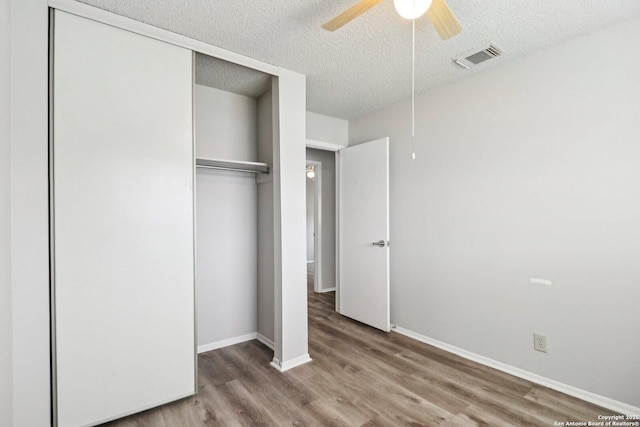 unfurnished bedroom with a closet, visible vents, a textured ceiling, wood finished floors, and baseboards