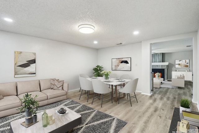 dining room with visible vents, a textured ceiling, wood finished floors, a warm lit fireplace, and baseboards