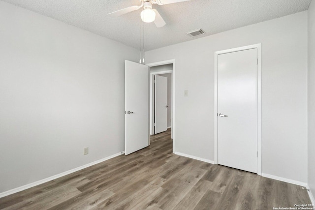 unfurnished bedroom with a textured ceiling, wood finished floors, visible vents, and baseboards