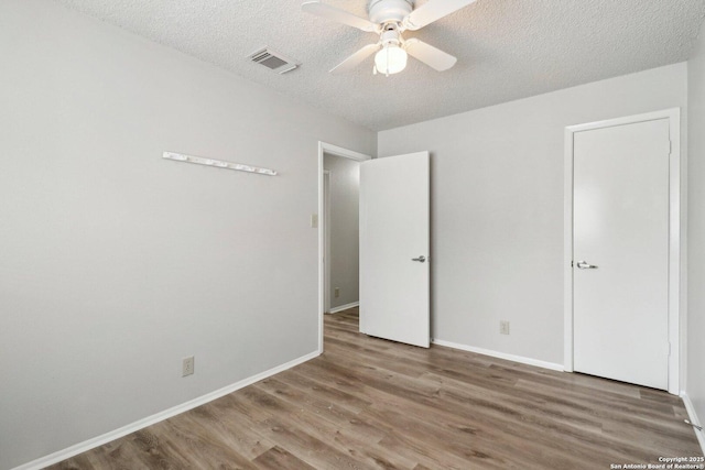 unfurnished bedroom with a textured ceiling, wood finished floors, visible vents, and baseboards