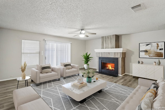 living room with a textured ceiling, wood finished floors, visible vents, baseboards, and a lit fireplace