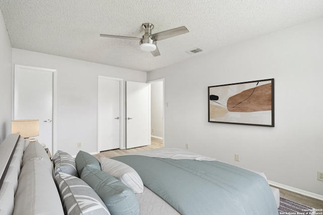 bedroom with a textured ceiling, visible vents, baseboards, a ceiling fan, and light wood-style floors