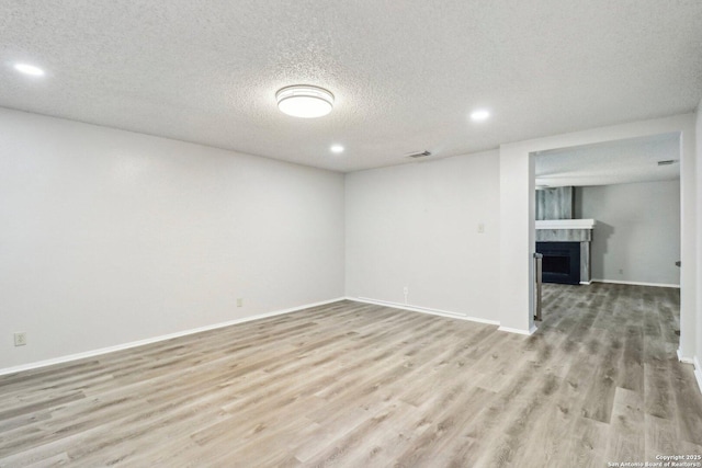 unfurnished room featuring visible vents, a fireplace, light wood-style flooring, and baseboards