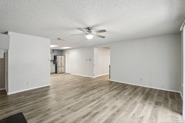 unfurnished living room with visible vents, ceiling fan, a textured ceiling, wood finished floors, and baseboards