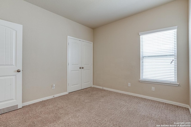 unfurnished bedroom with a closet, multiple windows, light carpet, and baseboards