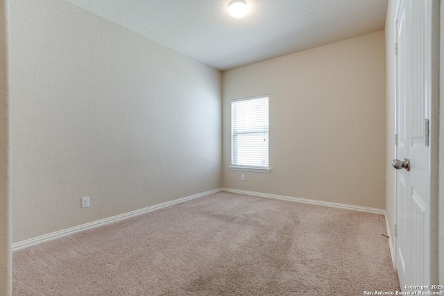 spare room with light colored carpet, a textured wall, and baseboards