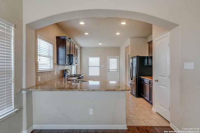 kitchen with light stone counters, arched walkways, dark brown cabinetry, and a peninsula