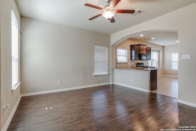 unfurnished living room featuring baseboards, visible vents, arched walkways, a ceiling fan, and dark wood-style floors