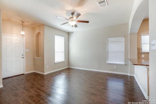 unfurnished living room featuring visible vents, arched walkways, dark wood finished floors, ceiling fan, and a textured ceiling