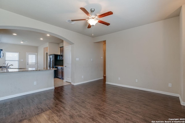 unfurnished living room featuring baseboards, visible vents, a ceiling fan, arched walkways, and dark wood-style flooring