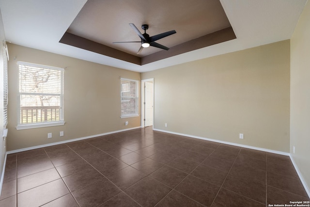 unfurnished room featuring baseboards, a raised ceiling, a ceiling fan, and dark tile patterned flooring