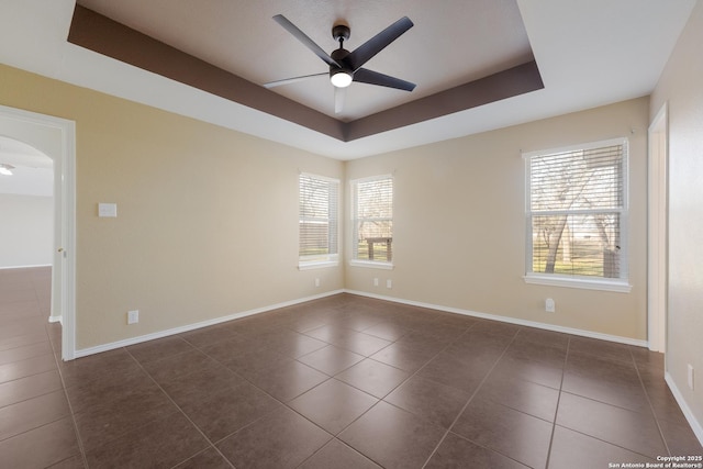 unfurnished room featuring arched walkways, dark tile patterned flooring, a tray ceiling, and a ceiling fan