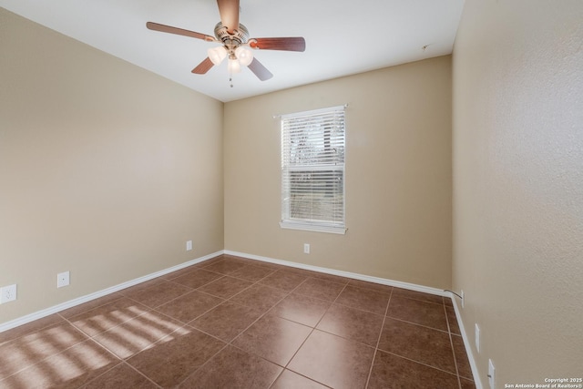 empty room with ceiling fan, dark tile patterned floors, and baseboards