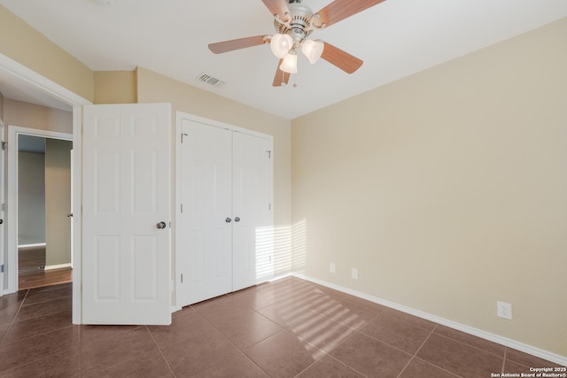 unfurnished bedroom featuring dark tile patterned flooring, a ceiling fan, visible vents, baseboards, and a closet