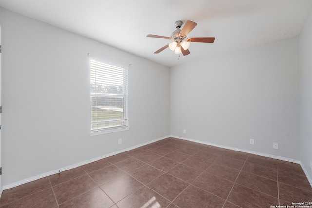 spare room featuring ceiling fan, dark tile patterned flooring, and baseboards