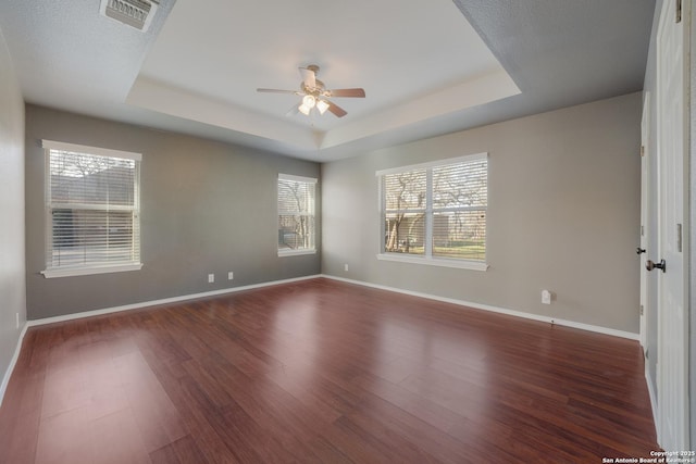 spare room with a tray ceiling, dark wood-style flooring, visible vents, and baseboards