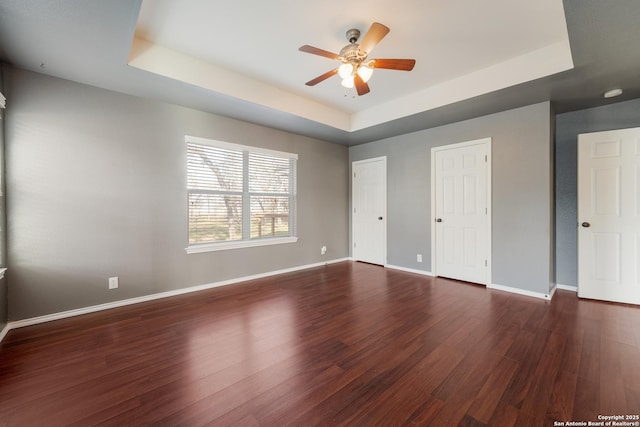 unfurnished bedroom featuring dark wood-style flooring, multiple closets, a raised ceiling, and baseboards