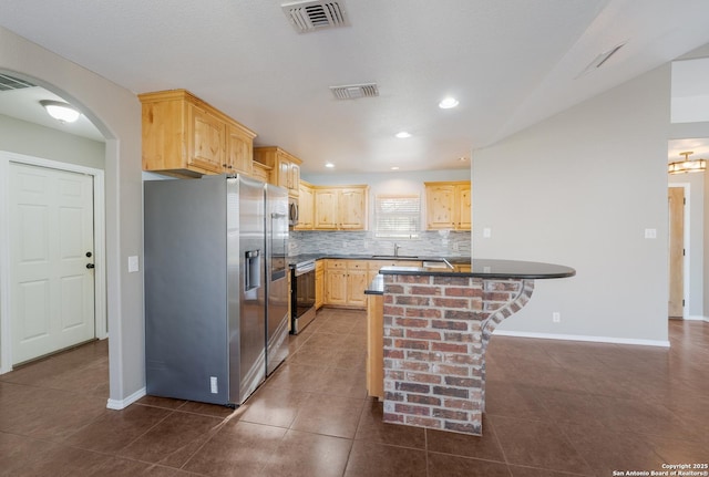 kitchen featuring dark countertops, decorative backsplash, light brown cabinetry, appliances with stainless steel finishes, and a kitchen bar