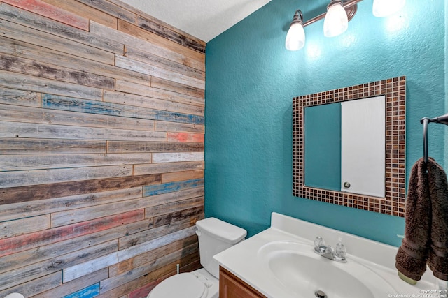 half bath featuring a textured wall, wooden walls, toilet, and vanity