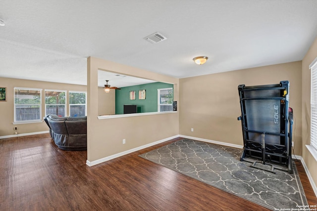 interior space with a ceiling fan, wood finished floors, visible vents, and baseboards