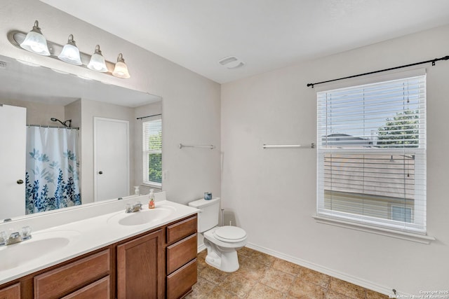 bathroom with baseboards, a sink, toilet, and double vanity