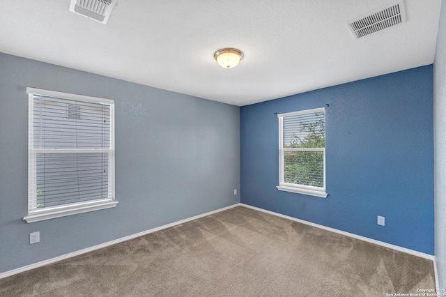 empty room with carpet flooring, visible vents, and baseboards