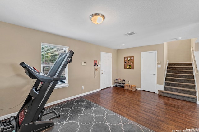 exercise area with dark wood-style flooring, visible vents, a textured ceiling, and baseboards