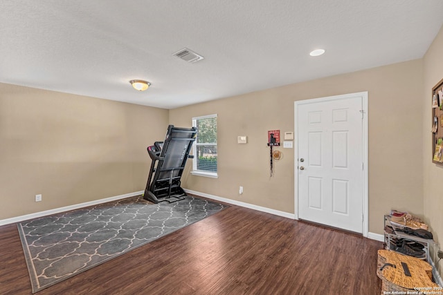 exercise area with dark wood-style floors, a textured ceiling, visible vents, and baseboards