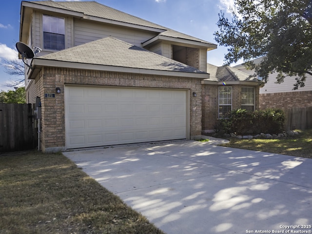 traditional-style house featuring an attached garage, a shingled roof, fence, and concrete driveway