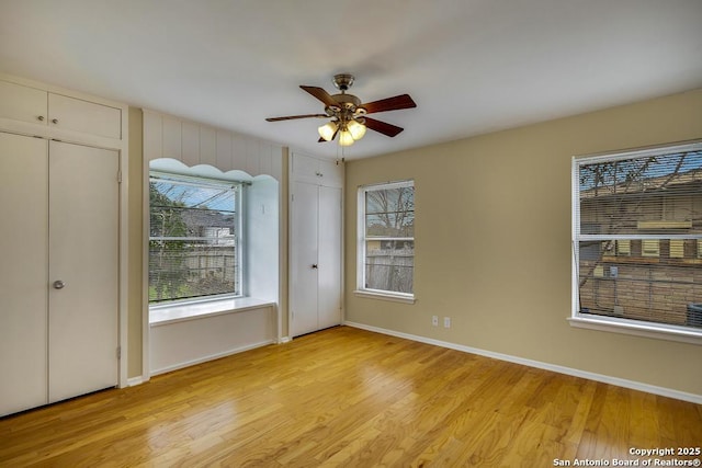 unfurnished bedroom with baseboards, light wood finished floors, and multiple closets