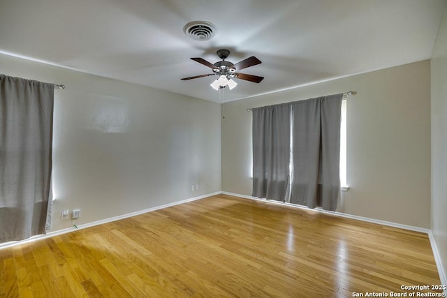 spare room with a ceiling fan, visible vents, baseboards, and wood finished floors