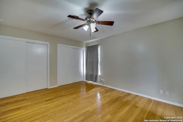 unfurnished bedroom with light wood-style flooring, baseboards, and two closets