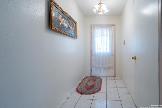 doorway to outside with a notable chandelier, baseboards, and light tile patterned floors