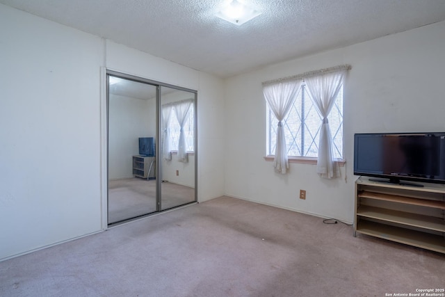 unfurnished bedroom featuring a textured ceiling, multiple windows, light carpet, and a closet