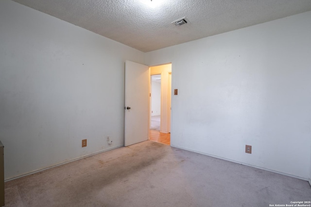 empty room with a textured ceiling, visible vents, and light colored carpet