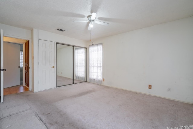 unfurnished bedroom featuring ceiling fan, a textured ceiling, light carpet, visible vents, and a closet