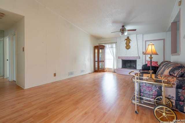 living area featuring a large fireplace, visible vents, ceiling fan, a textured ceiling, and light wood-style floors