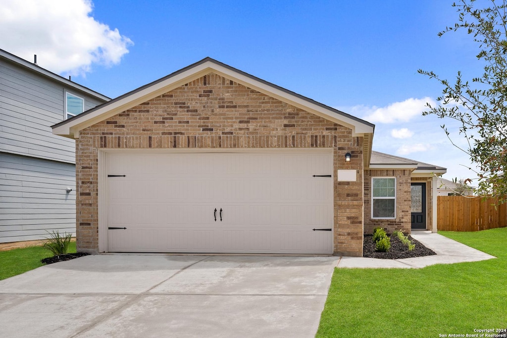 view of front of house featuring brick siding, an attached garage, a front yard, fence, and driveway