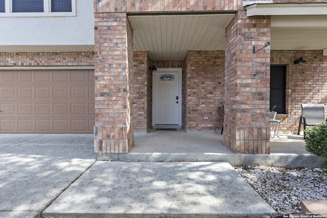 entrance to property with driveway, brick siding, and an attached garage