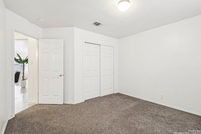 unfurnished bedroom with baseboards, visible vents, dark carpet, and a closet